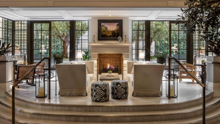 The raised fireplace area in Palm Court, framed by black-framed glazing onto the winter garden, Kimpton Fitzroy London