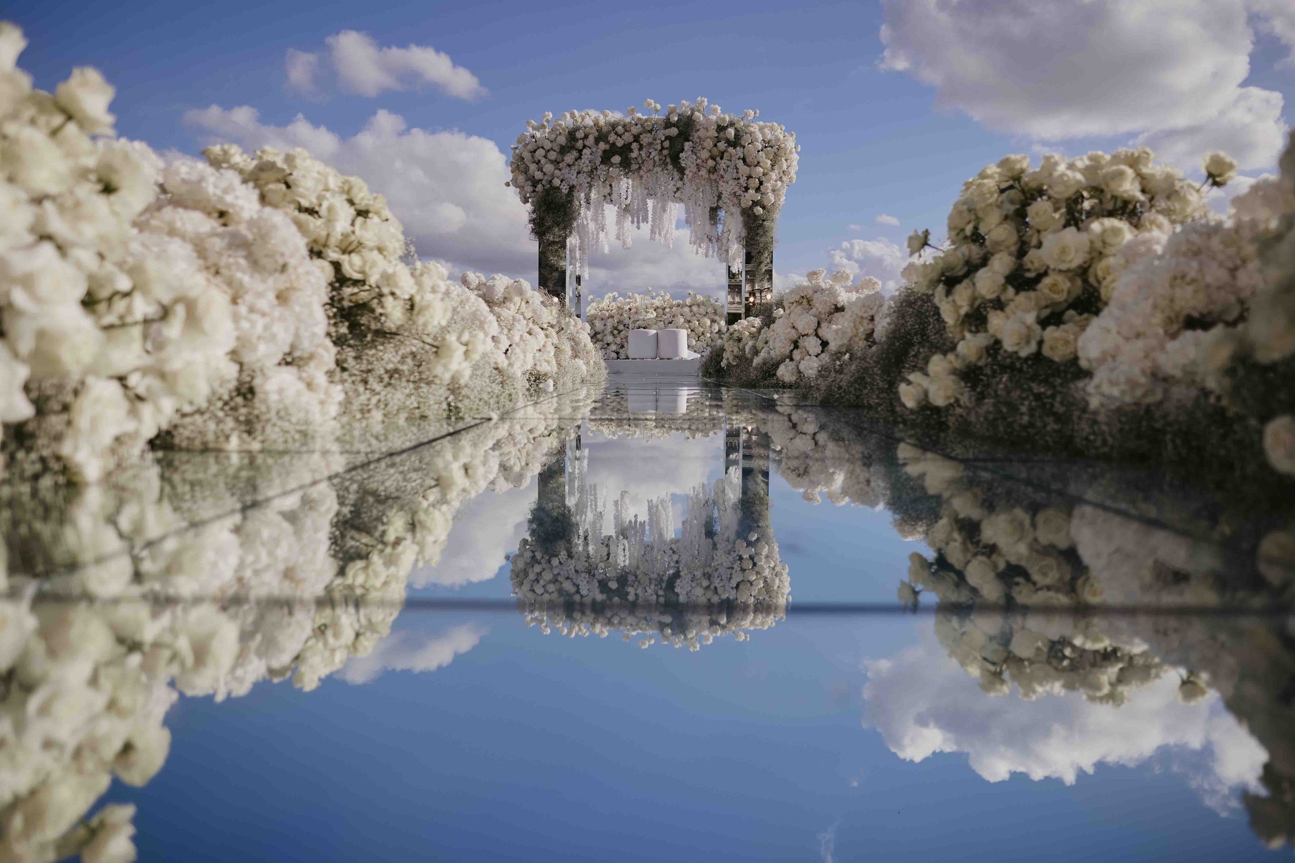 A wedding aisle of white flowers over a mirrored platform, KM Events
