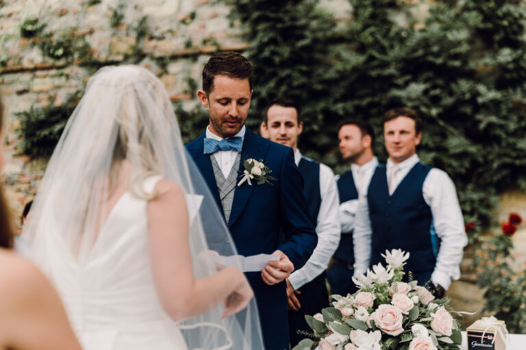 Vows beside an ivy-covered wall with the groomsmen looking on, Tuscany, La Bottega del Sogno