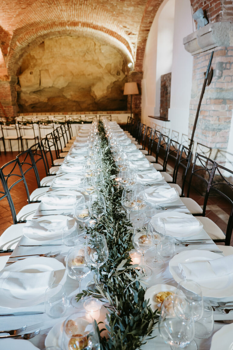 A long table dressed with olive foliage and candles beneath brick vaulting, Tuscany, La Bottega del Sogno