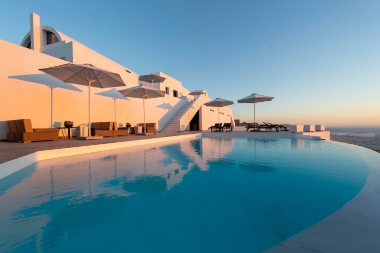 The pool and the whitewashed hotel at golden hour, double loungers and parasols along the water, La Maltese Estate