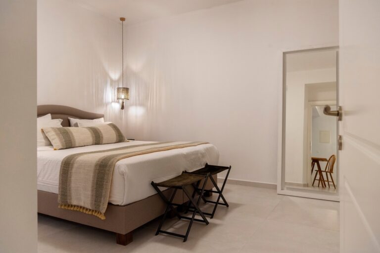 A suite bedroom in soft neutrals, a linen-dressed bed with a striped throw and a slim pendant, La Maltese Estate