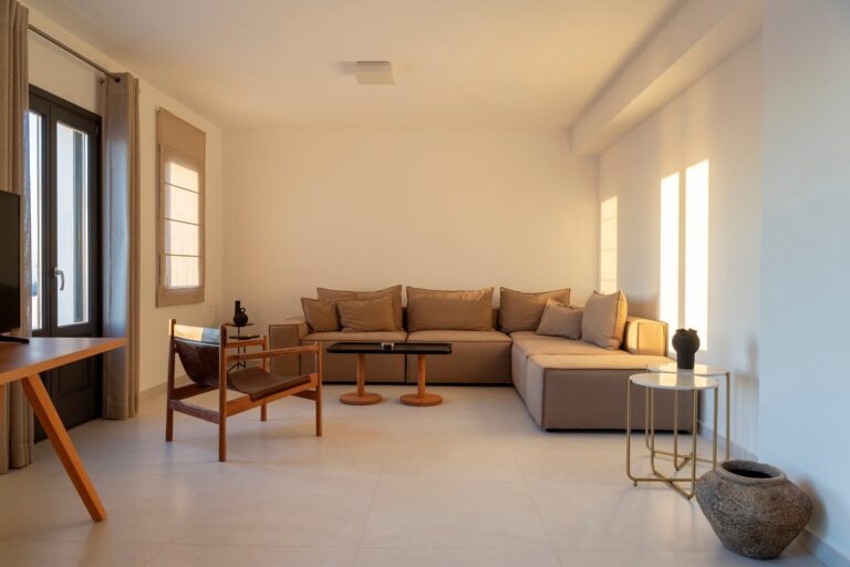 A suite sitting room, a low modular sofa in oatmeal linen, wood and stone against white walls, La Maltese Estate