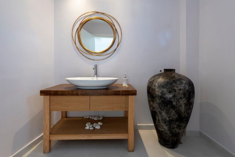 A bathroom vanity, a round gilt mirror above a stone basin, an antique amphora alongside, La Maltese Estate