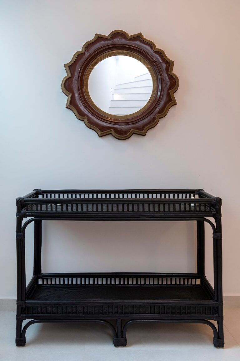 A black rattan console beneath a carved sunburst mirror, the light off the white walls, La Maltese Estate