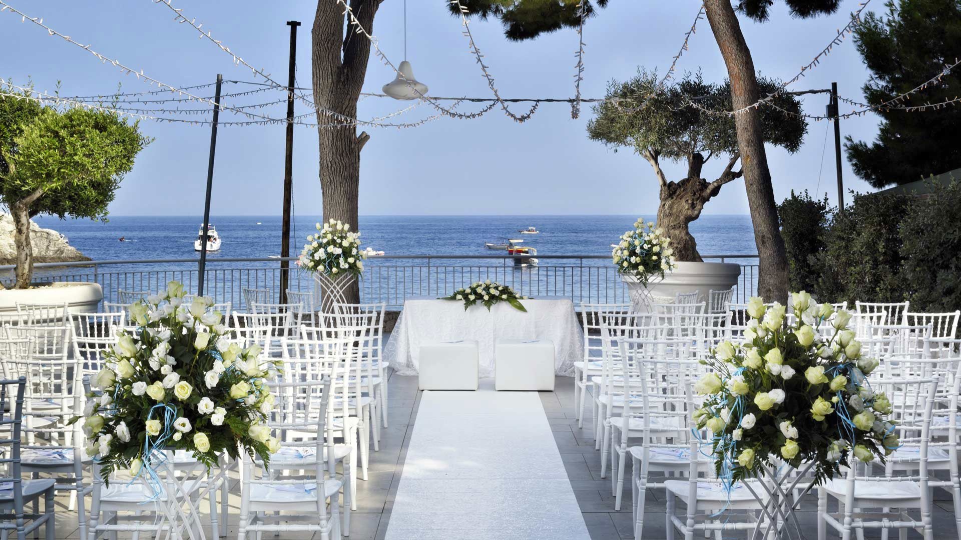 An outdoor wedding ceremony, a white aisle and florals facing the sea and Isola Bella, La Plage Resort
