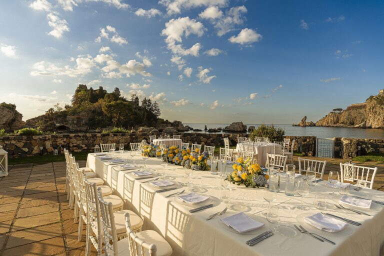 A wedding banquet table at golden hour, yellow and white flowers and the sea beyond, La Plage Resort