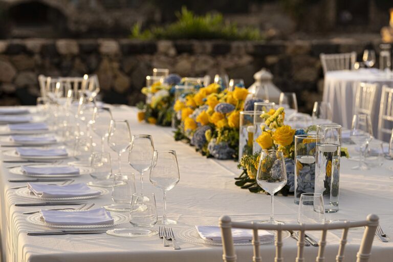A wedding tablescape in close-up, yellow blooms and glassware along a long table, La Plage Resort