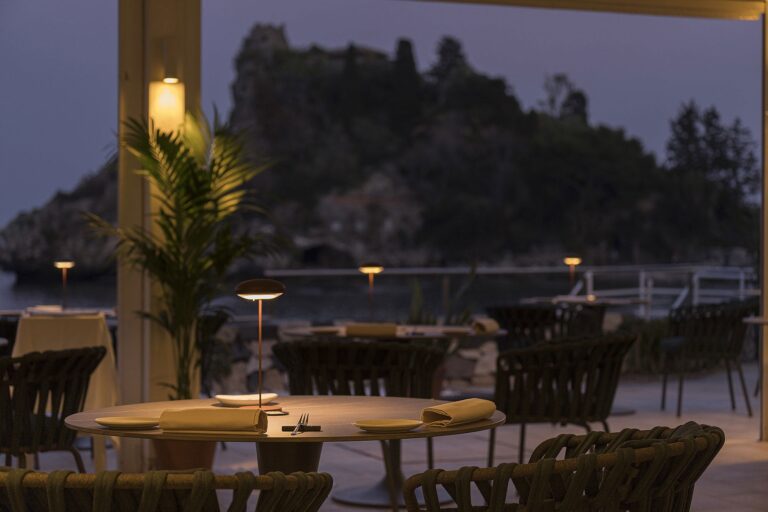 The Idda restaurant terrace at dusk, tables lit and Isola Bella beyond, La Plage Resort