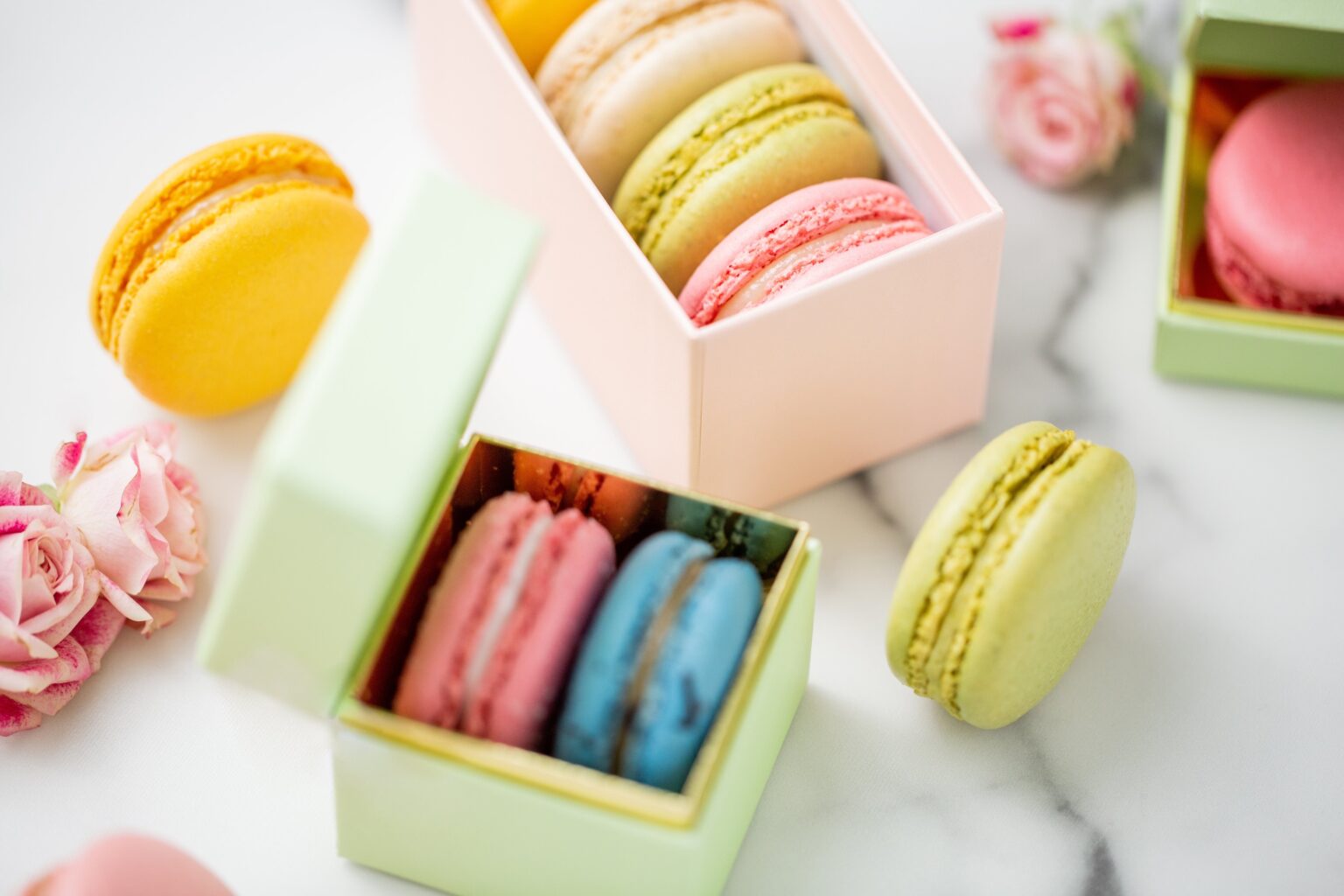 Small macaron boxes in pink and green on marble, suited to favours