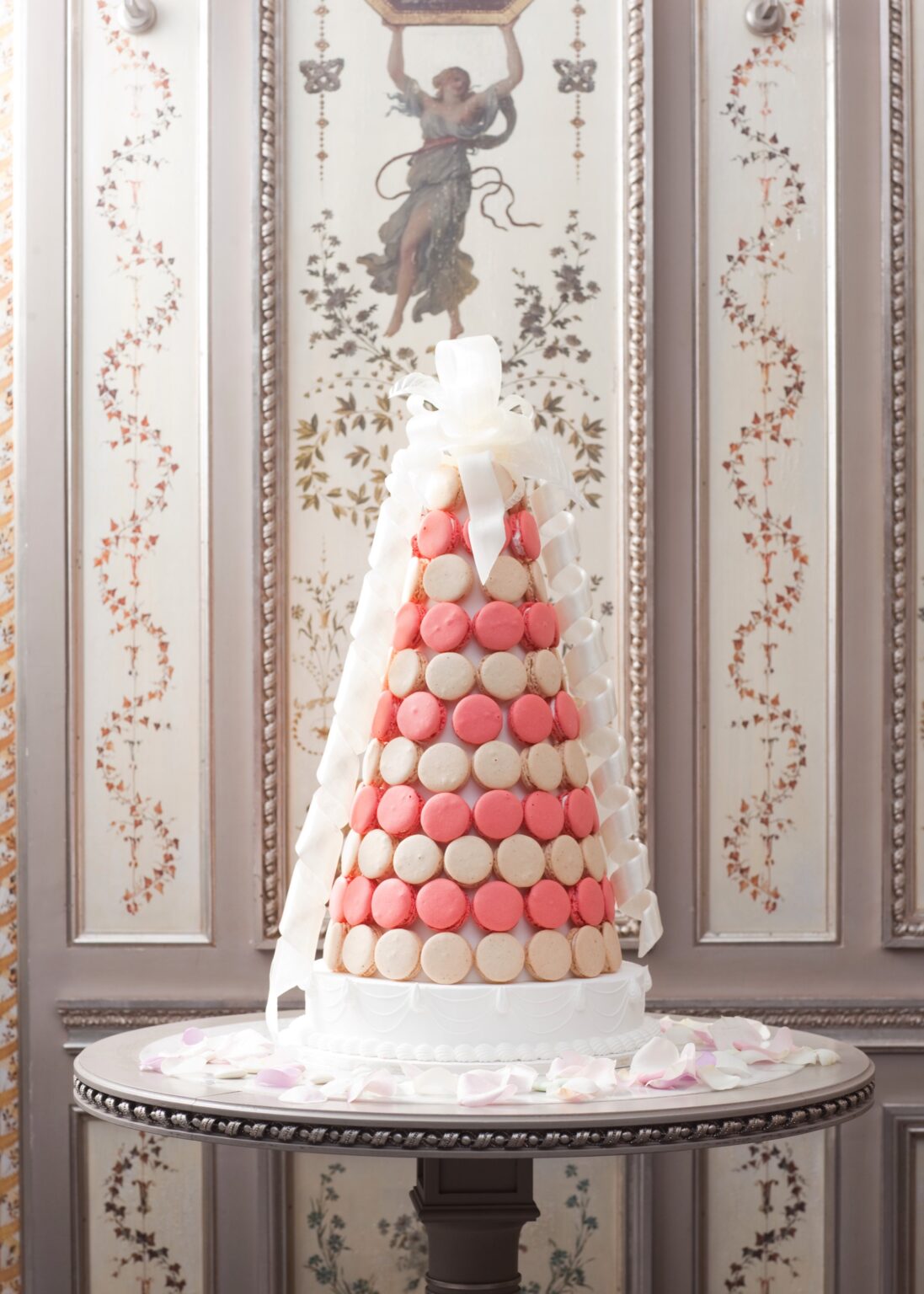 A macaron pyramid on a pedestal table in a Paris salon, petals scattered around the base