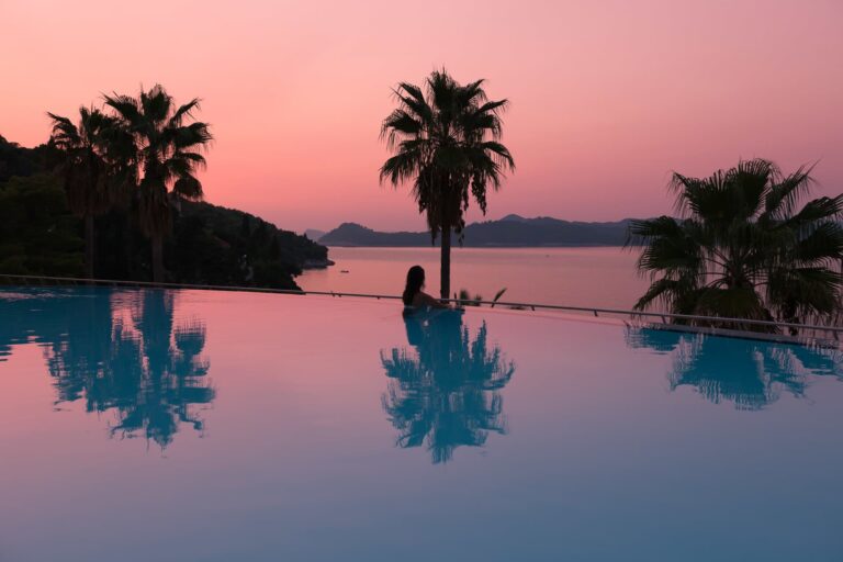 The infinity pool at sunset, a single figure in the water beneath palms and a rose-coloured sky, Lafodia Sea Resort