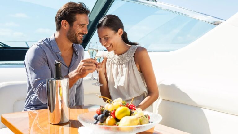 A couple toasting with champagne aboard a boat, fruit and flowers on the table between them, Lafodia Sea Resort