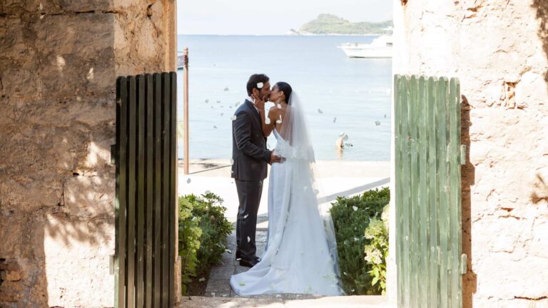 A bride and groom kissing in an old stone doorway, the beach and the sea framed beyond, Lafodia Sea Resort