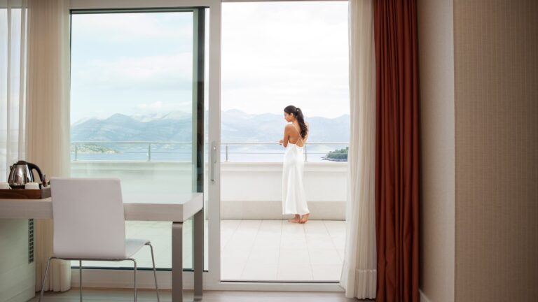 A guest at the open doors of a suite, looking out to the mountains across the sea, Lafodia Sea Resort