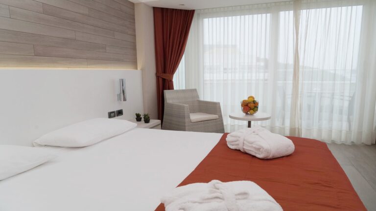 A Deluxe room dressed with robes on the bed and a private terrace beyond the glass, Lafodia Sea Resort