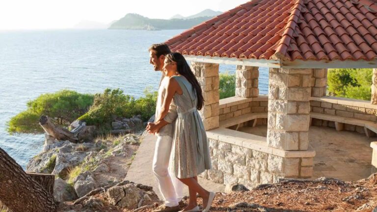 A couple by a stone gazebo on the cliff edge, the sea far below and the coast in the distance, Lafodia Sea Resort
