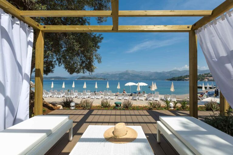 A beach cabana with white drapes and loungers, framing the pebble beach and the bay beyond, Lafodia Sea Resort