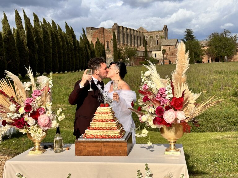 A toast beside a millefoglie wedding cake and burgundy and dried flowers on a lawn, the abbey and cypresses behind, Tuscany, Lake Maggiore & Tuscany Weddings