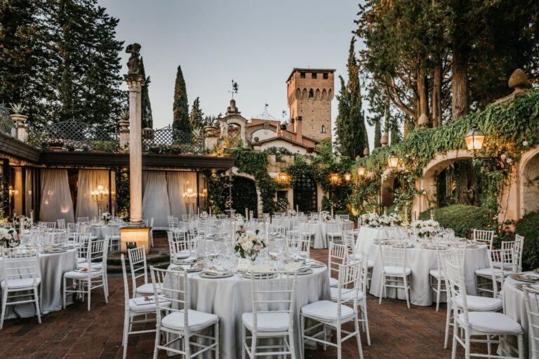 Round dinner tables on a brick terrace at dusk below a medieval tower and cypresses, Lake Maggiore, Lake Maggiore & Tuscany Weddings