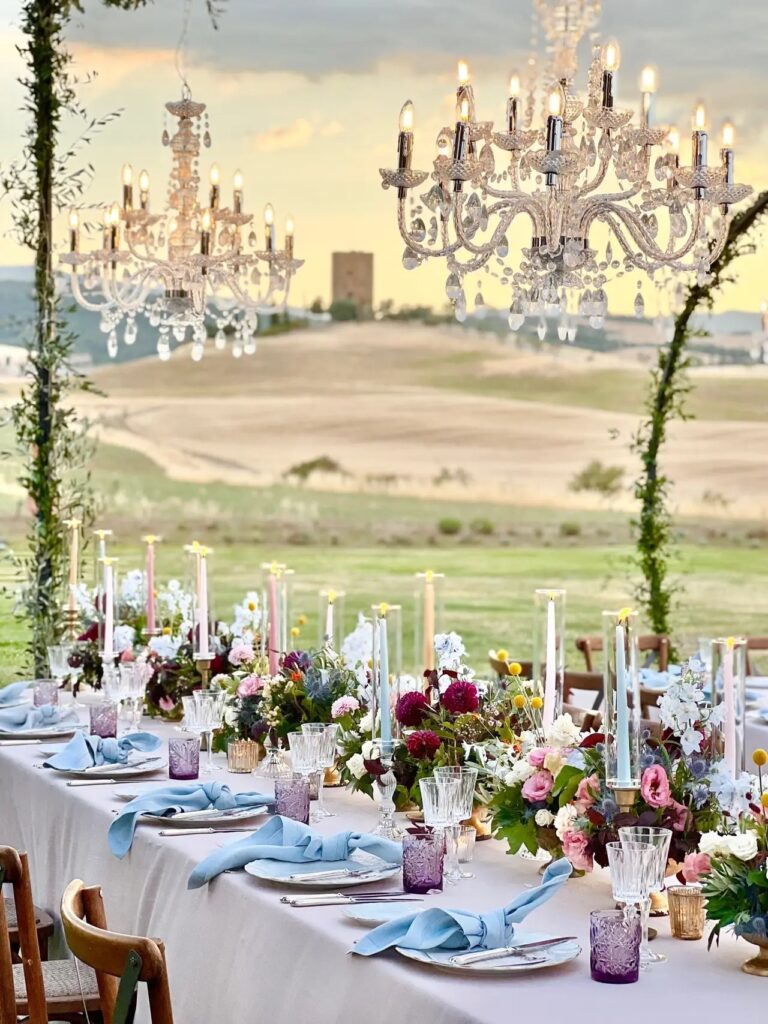 Crystal chandeliers hung over a long table set with blue napkins and mixed flowers, the Tuscan hills beyond, Lake Maggiore & Tuscany Weddings
