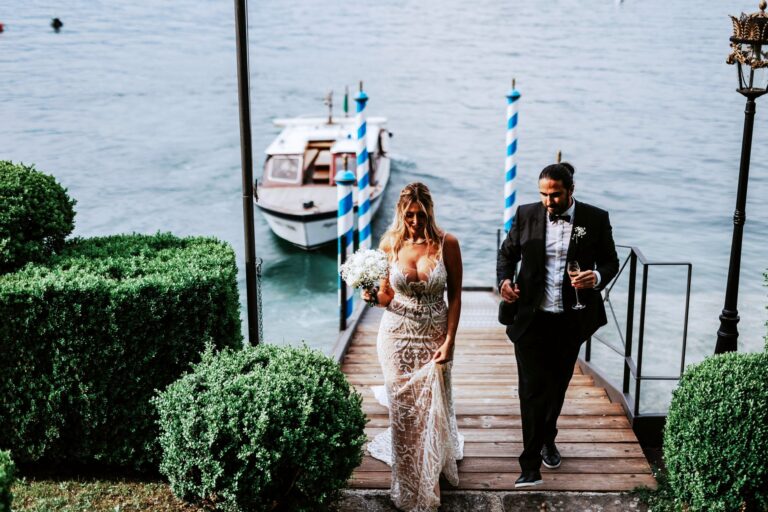 The couple walking up a wooden jetty past box hedges, a launch moored at blue and white poles, Lake Maggiore, Lake Maggiore & Tuscany Weddings