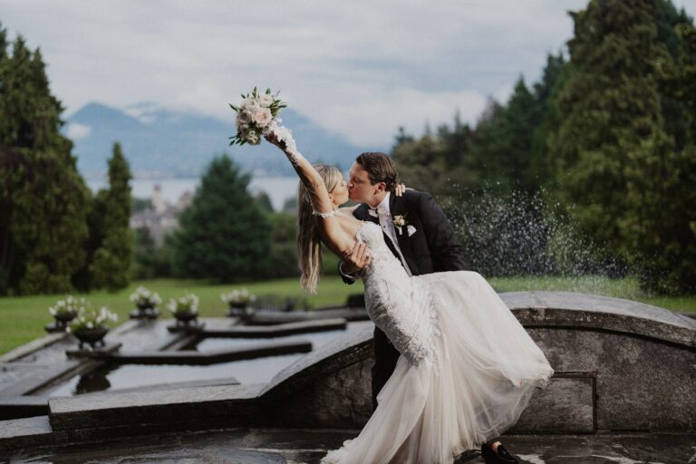 The couple in a dip beside a formal water parterre, bouquet raised, the lake and mountains behind, Lake Maggiore, Lake Maggiore & Tuscany Weddings