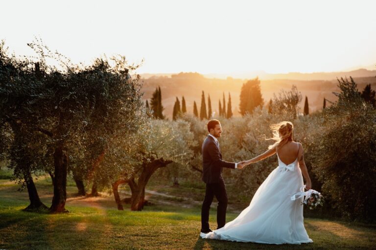 The couple hand in hand in an olive grove at sunset, cypresses on the ridge behind, Tuscany, Lake Maggiore & Tuscany Weddings