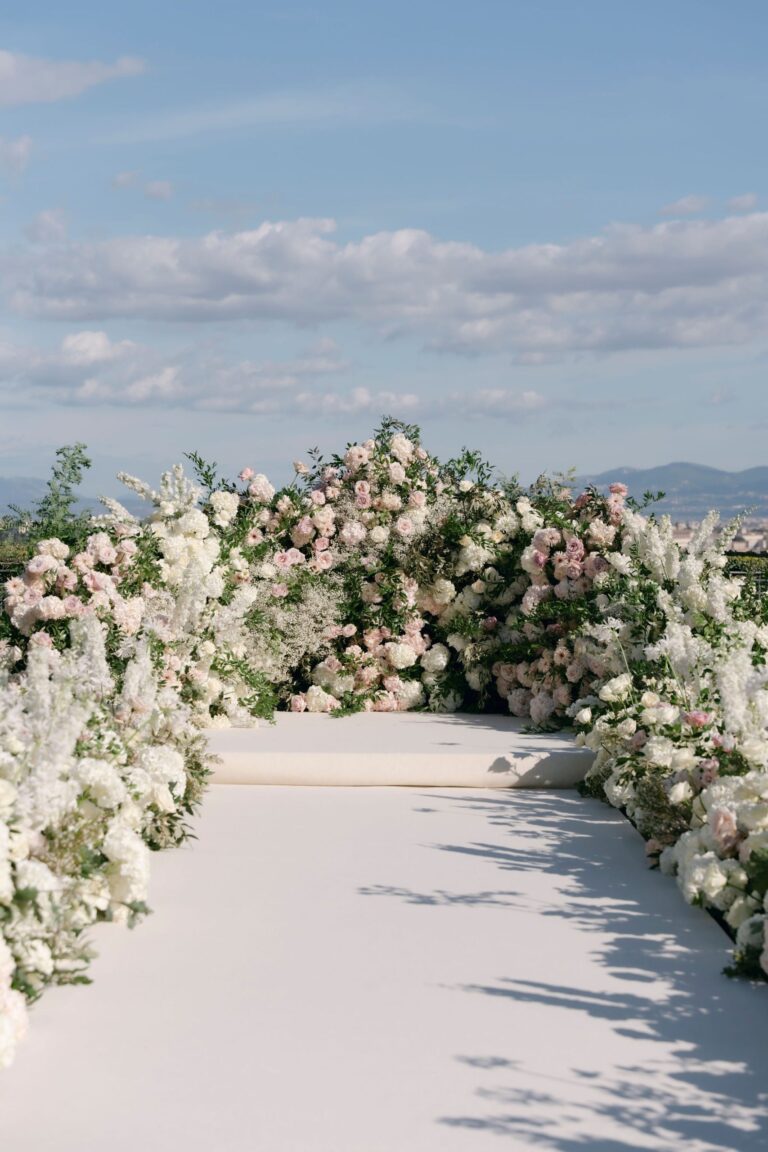 A white aisle lined with banks of white and blush roses on a hilltop terrace, Le Rêve