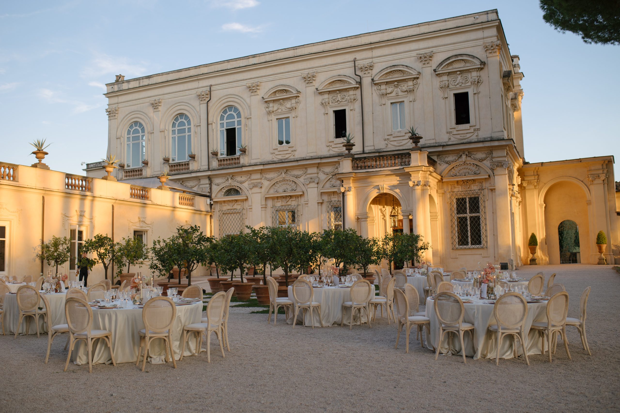 Round dinner tables set in a gravel courtyard before a Renaissance villa at sunset, Rome, Le Rêve