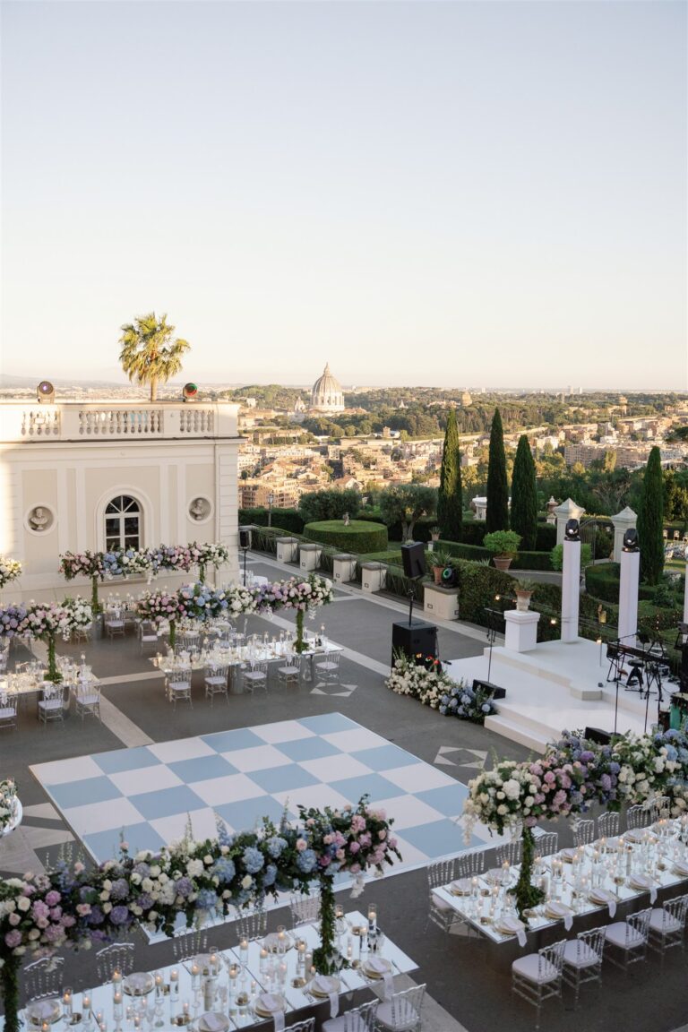 A terrace laid for dinner with a chequerboard dance floor and flower-lined tables, Rome's rooftops and St Peter's behind, Le Rêve