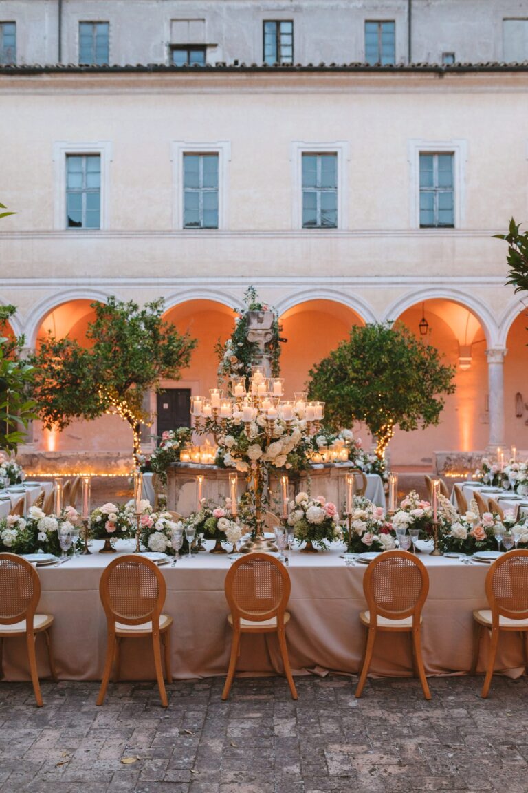 A long dinner table in an arcaded courtyard, potted lemon trees and candelabra set along it, Le Rêve