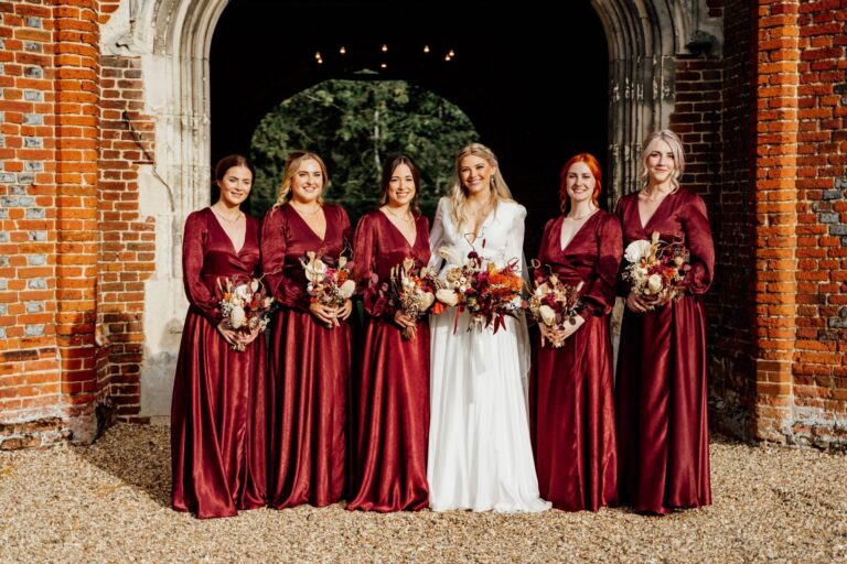 The bride with her bridesmaids in wine-red gowns, gathered in the brick archway of the Tower, Leez Priory