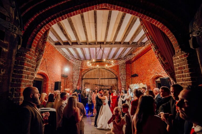 A first dance in the Coach House at night, guests gathered beneath fairy lights and a great timber arch, Leez Priory