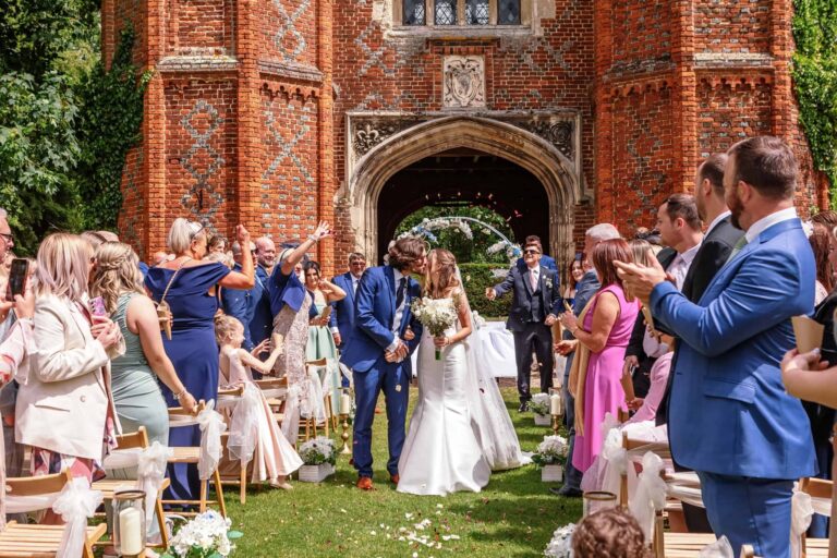 The couple kissing under a fall of confetti as they leave their outdoor ceremony beneath the Tower, Leez Priory