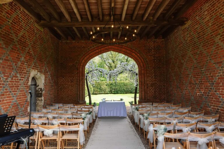 A covered brick ceremony space, its pointed arch opening onto the garden and a blossom tree, Leez Priory