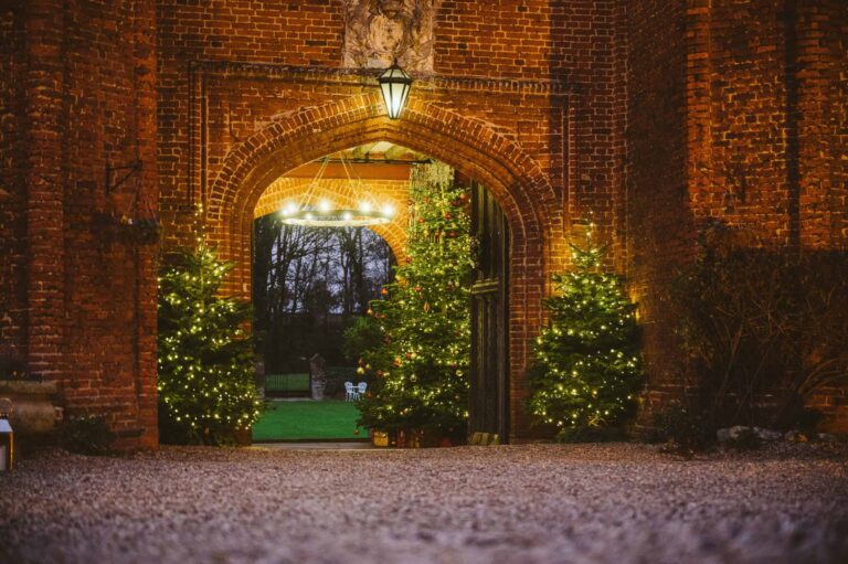 The carriageway arch at dusk, lit Christmas trees framing the way through to the garden beyond, Leez Priory