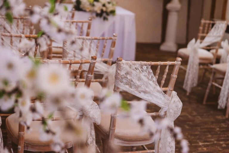 A ceremony detail, chiavari chairs dressed with lace sashes and blossom, Leez Priory