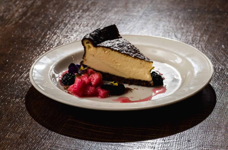 A slice of baked vanilla cheesecake plated with rhubarb, blackberries and edible flowers, Leez Priory