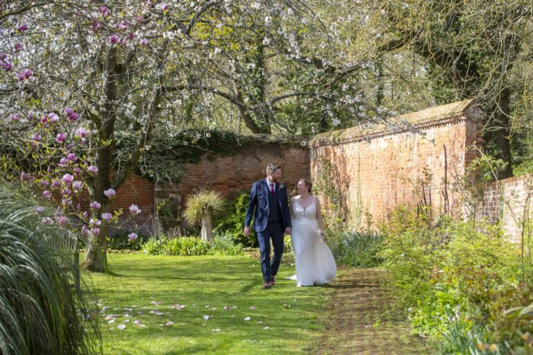The couple walking a grass path through the walled garden, beneath a magnolia in bloom, Leez Priory