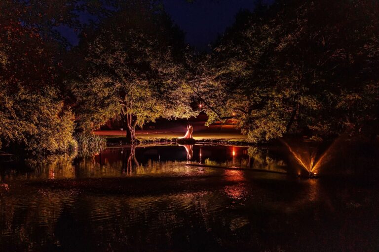 The couple lit across the lake at night, reflections and a floodlit fountain in the water, Leez Priory
