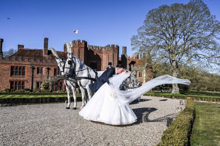 The couple kissing beside a white horse-drawn carriage on the gravel before the house, Leez Priory