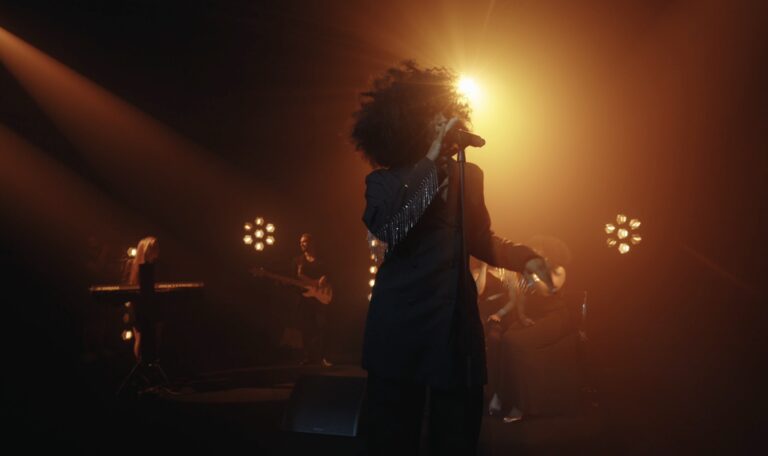 A singer silhouetted by a warm spotlight on stage, Les Cigales