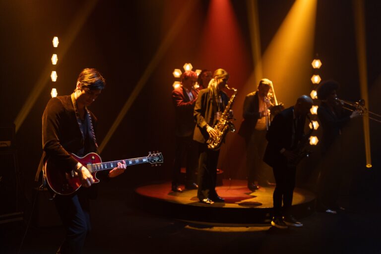 The band on stage with guitar and saxophone under amber and red lights, Les Cigales