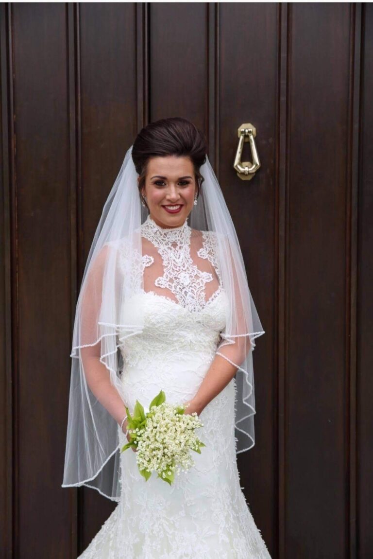 Bride in a high-necked lace gown and veil holding lily of the valley, Lesley Cutler Bridal Wear