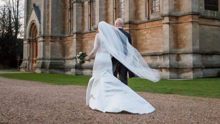 Bride with her veil lifting in the wind outside a stone church, Lesley Cutler Bridal Wear