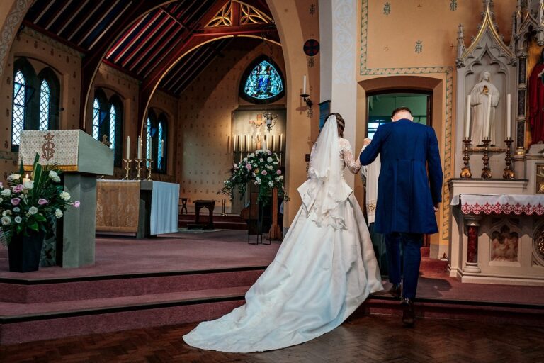 Bride with a long train at the altar of a church, Lesley Cutler Bridal Wear