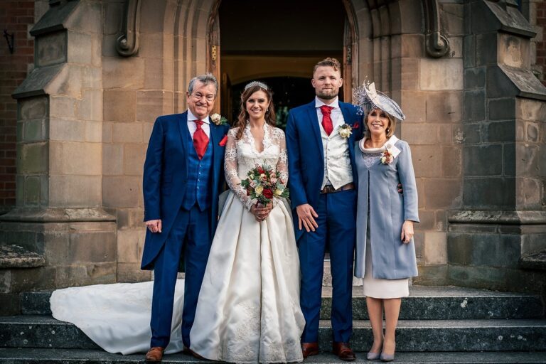 Bride on church steps with her party, her train spread behind her, Lesley Cutler Bridal Wear