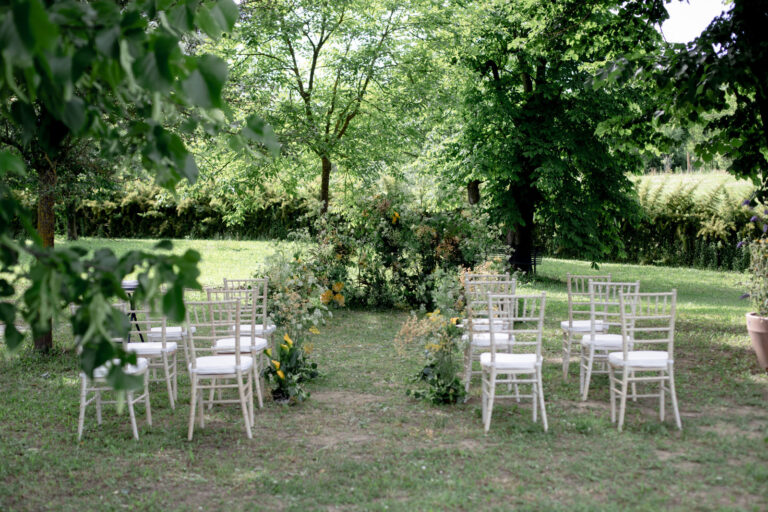 Ceremony chairs set out on a lawn among trees and flowering shrubs, Letizia T. Events