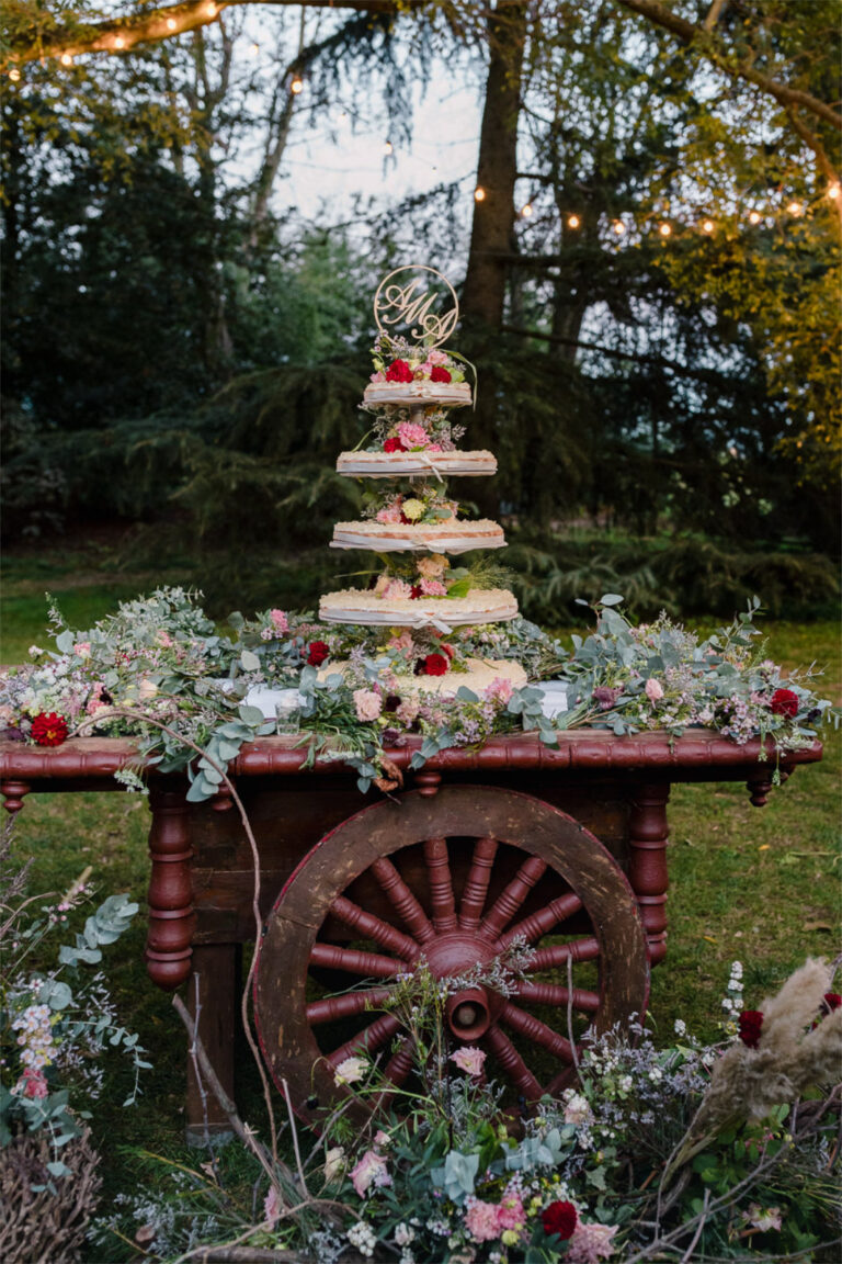 Wedding cake on a rustic cart covered in flowers, lit in the evening garden, Letizia T. Events